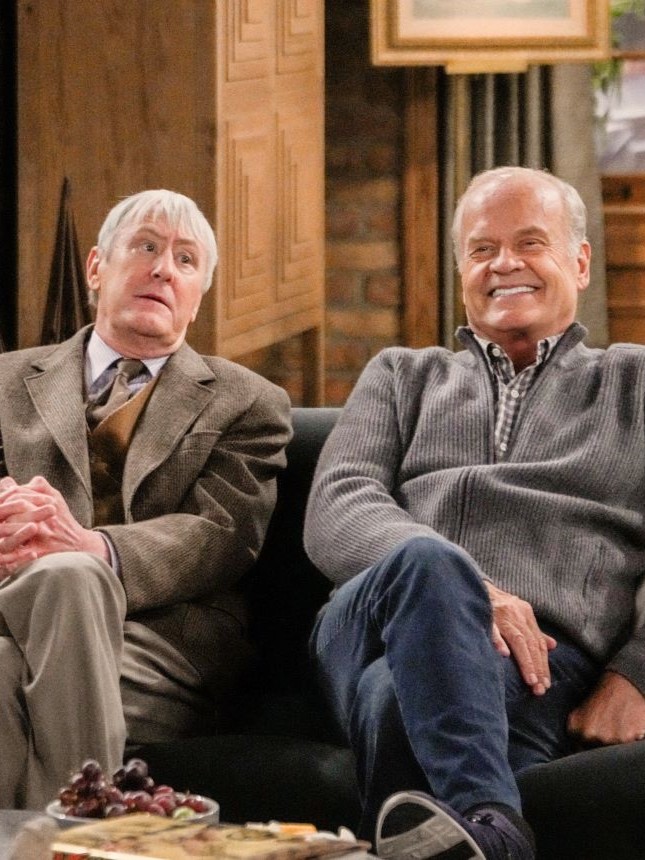 Frasier and Alan sit side by side on the sofa