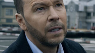 Danny standing in an empty parking lot looking at something on Blue Bloods Season 14 Episode 11