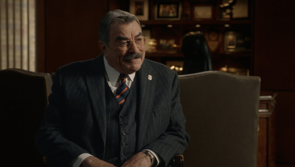 Frank sitting and wearing a suit with a red and blue striped tie on Blue Bloods Season 14 Episode 11