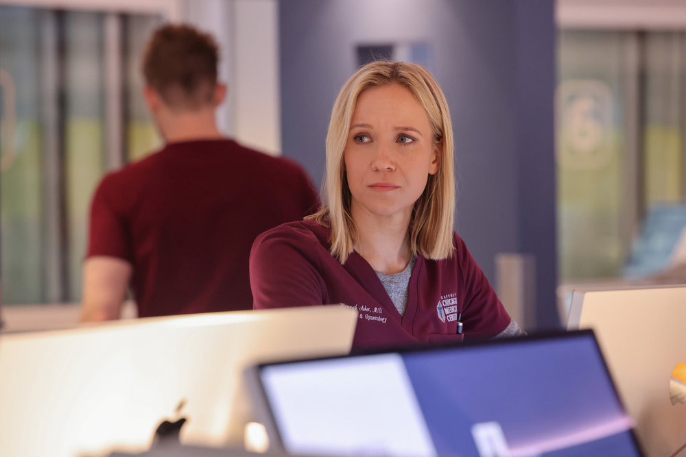 Hannah standing at her desk looking sad on Chicago Med Season 10 Episode 22