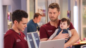 Frost and Ripley stand by the nurse's station on Chicago Med Season 10 Episode 21. Ripley is holding a baby.