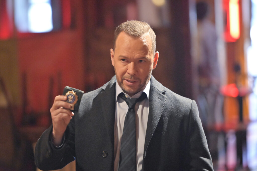 Danny holds up his badge against a blurry background on Blue Bloods/Boston Blue