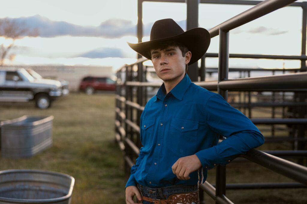 Alex leaning against a fence on My Life With The Walter Boys Season 2