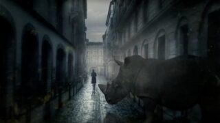 A woman walks down a foggy cobblestone street as a rhinoceros emerges from the shadows beside her, in a surreal scene from the Zoo TV series.