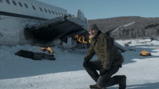 A US marshal on one knee before a crashed plane on a snowy vista