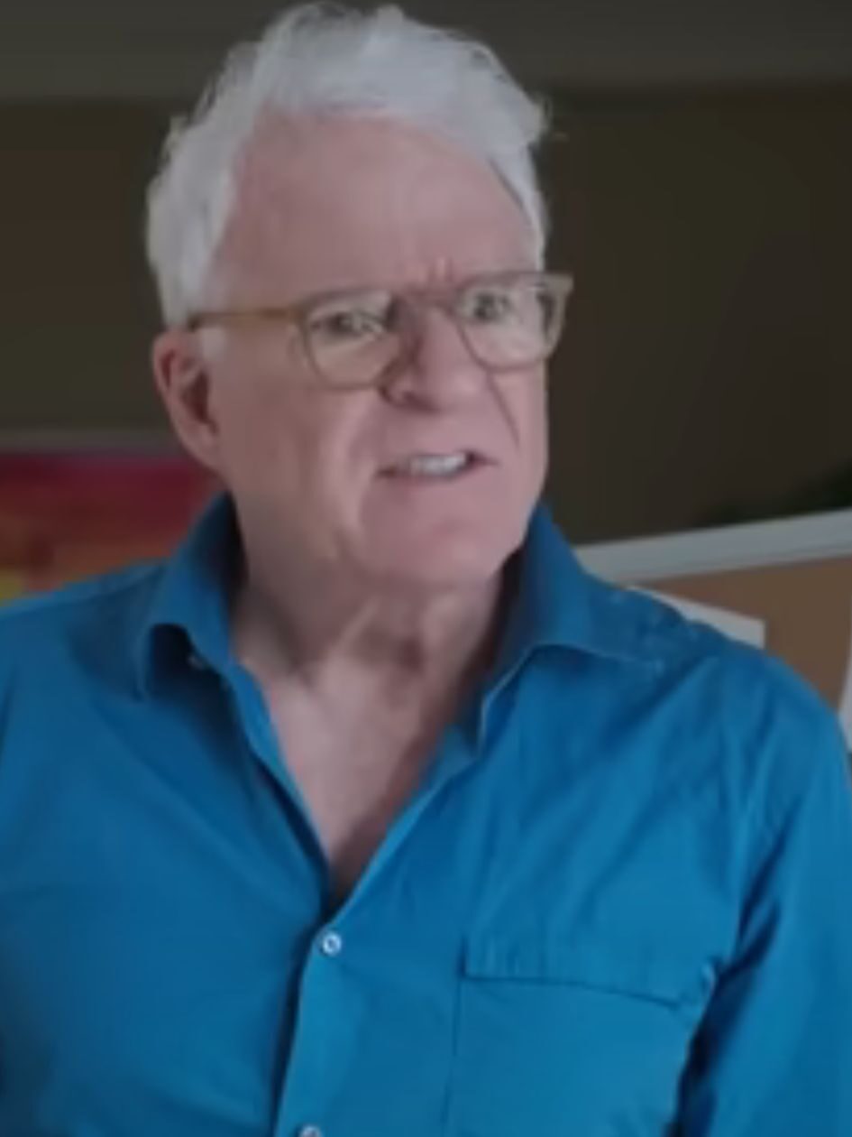 Charles stand by the corkboard wearing a blue shirt on Only Murders In The Building Season 5