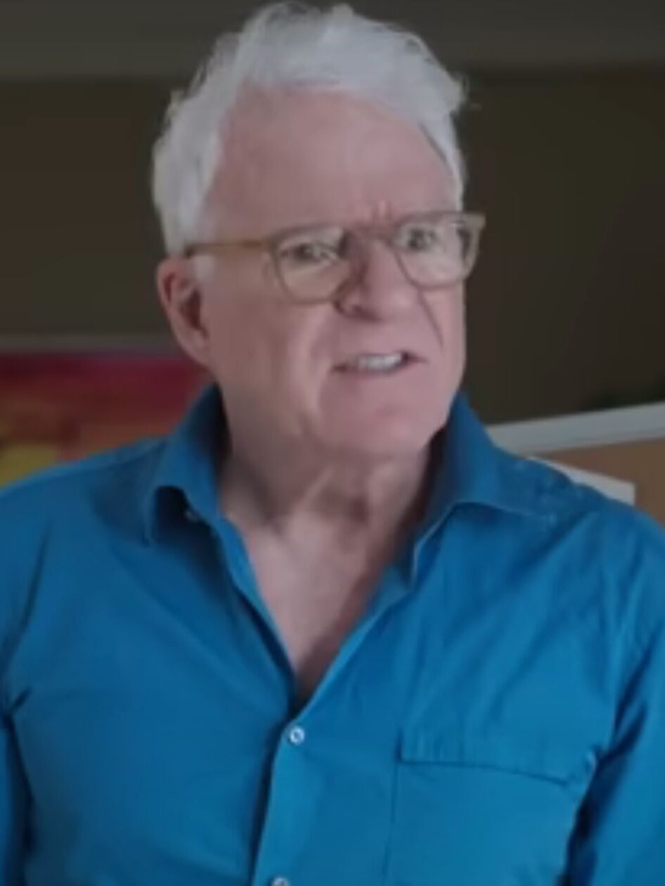 Charles stand by the corkboard wearing a blue shirt on Only Murders In The Building Season 5