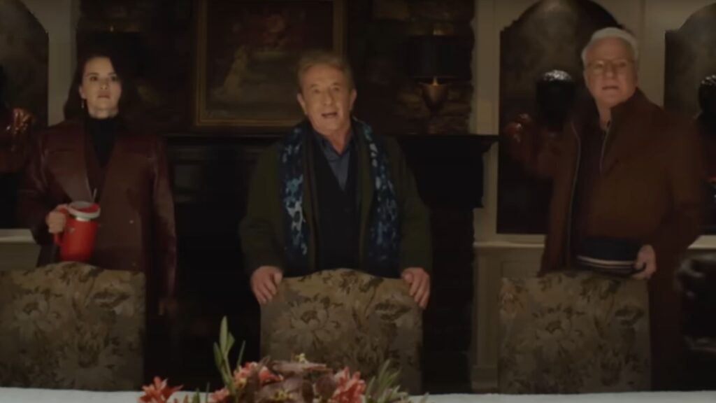 The trio stands behind their chairs and look scared at something offscreen on Only Murders In The Building Season 5.