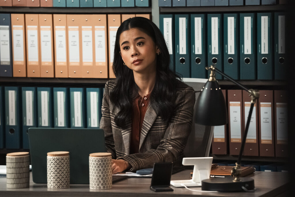 Sarah sentada atrás de uma mesa parecendo presunçosa no episódio 7 da 2ª temporada de Matlock