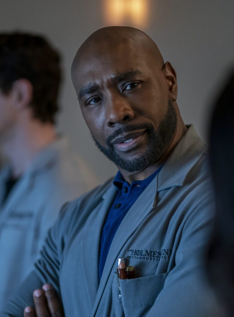 Watson crosses his arms and thinks about a problem on Watson Season 2 Episode 12